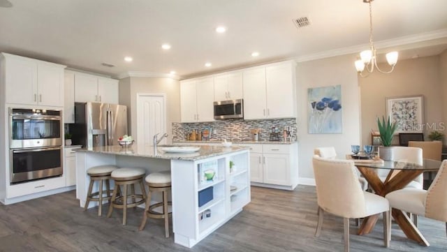 kitchen featuring appliances with stainless steel finishes, pendant lighting, white cabinetry, light stone counters, and a center island with sink