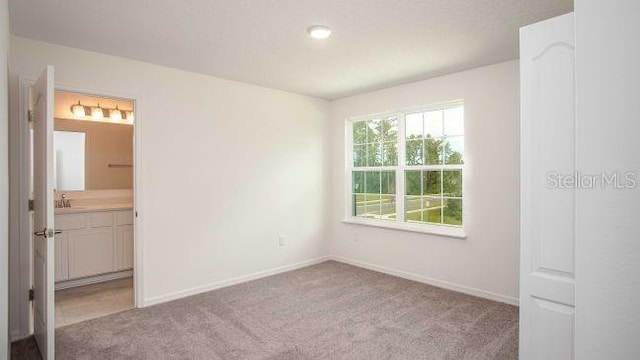 unfurnished bedroom featuring a sink, ensuite bathroom, baseboards, and carpet floors