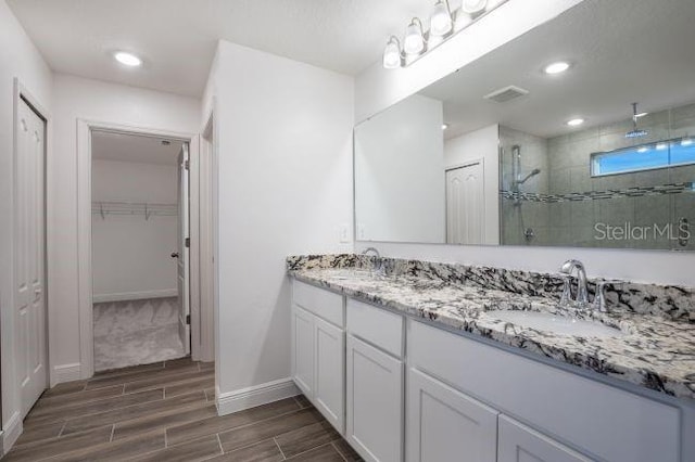 full bath with wood tiled floor, visible vents, a tile shower, and a sink