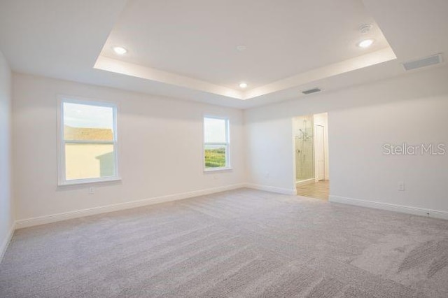 spare room with a tray ceiling, recessed lighting, light colored carpet, and baseboards