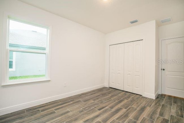 unfurnished bedroom featuring visible vents, baseboards, a closet, and wood tiled floor