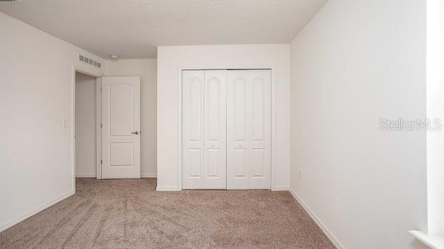 unfurnished bedroom with visible vents, a textured ceiling, a closet, carpet, and baseboards