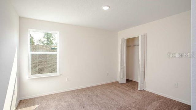 unfurnished bedroom featuring light carpet, a closet, and baseboards