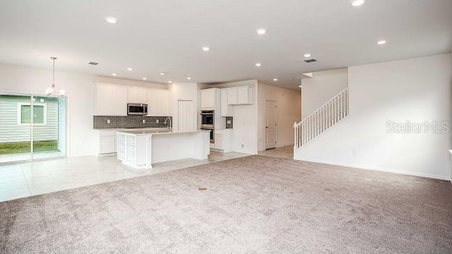 kitchen featuring a kitchen island with sink, tasteful backsplash, open floor plan, white cabinetry, and appliances with stainless steel finishes