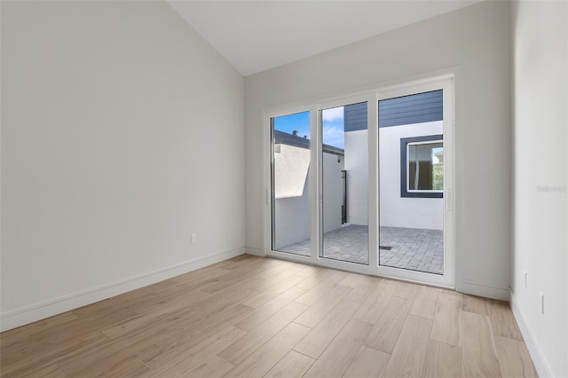 spare room featuring light wood-type flooring and vaulted ceiling