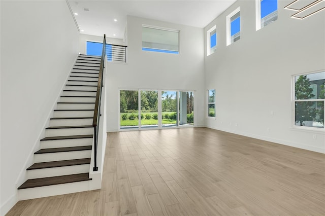 unfurnished living room featuring a towering ceiling and light hardwood / wood-style flooring