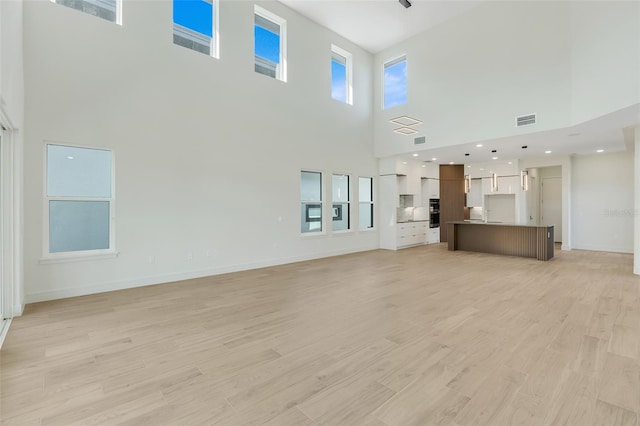 unfurnished living room with a towering ceiling and light hardwood / wood-style flooring