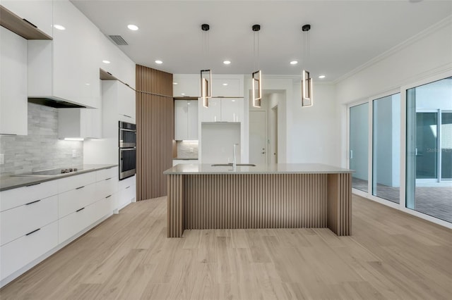 kitchen with pendant lighting, white cabinetry, decorative backsplash, sink, and a center island with sink