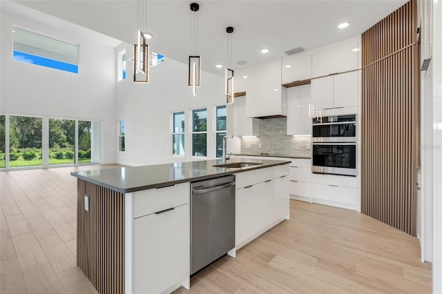 kitchen featuring hanging light fixtures, white cabinets, a center island with sink, and stainless steel appliances