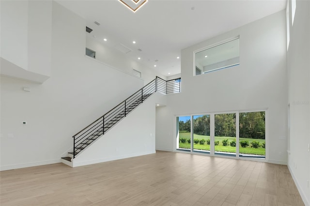 unfurnished living room featuring a towering ceiling and light hardwood / wood-style flooring