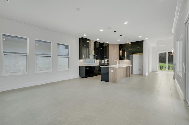 kitchen featuring pendant lighting, decorative backsplash, a center island with sink, crown molding, and wall chimney range hood