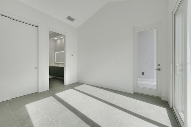 unfurnished bedroom with vaulted ceiling, connected bathroom, and light tile patterned flooring