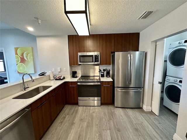 kitchen with light hardwood / wood-style flooring, stacked washer / dryer, appliances with stainless steel finishes, and sink