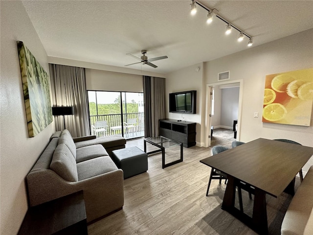 living room featuring rail lighting, light hardwood / wood-style floors, ceiling fan, and a textured ceiling