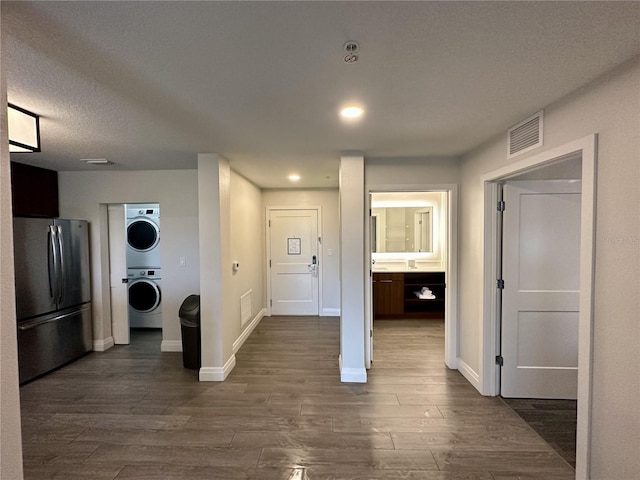 kitchen with stainless steel fridge, stacked washer / drying machine, a textured ceiling, and dark hardwood / wood-style flooring