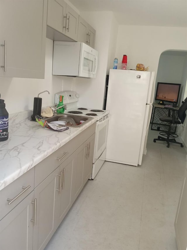 kitchen featuring gray cabinetry, light tile floors, light stone countertops, and white appliances