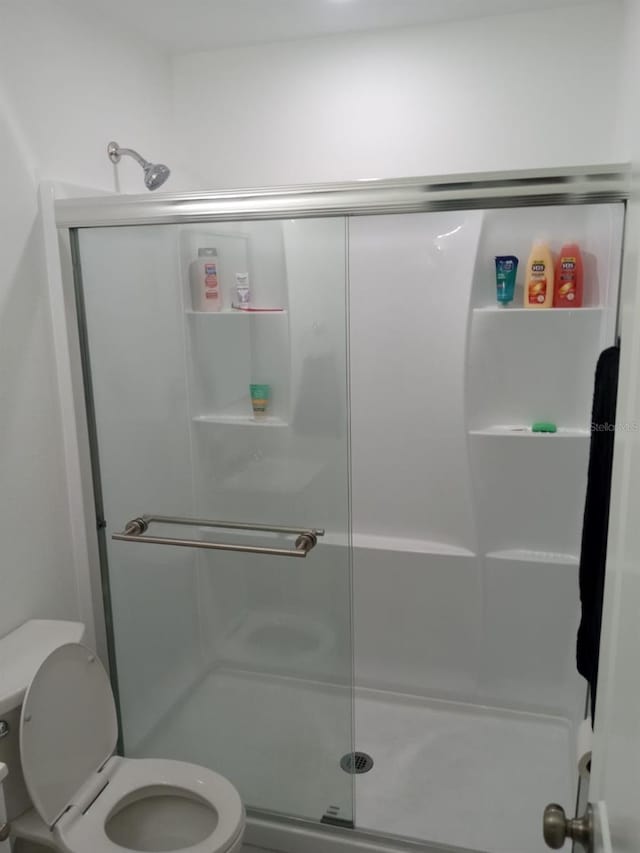 bathroom featuring a shower with door and toilet