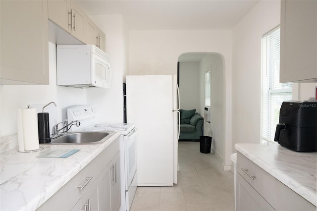 kitchen with white appliances, sink, light tile floors, and light stone countertops