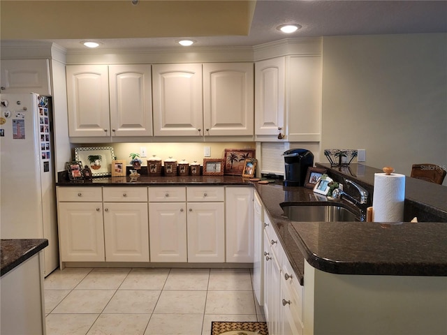 kitchen featuring white refrigerator, light tile flooring, white cabinetry, dark stone countertops, and sink