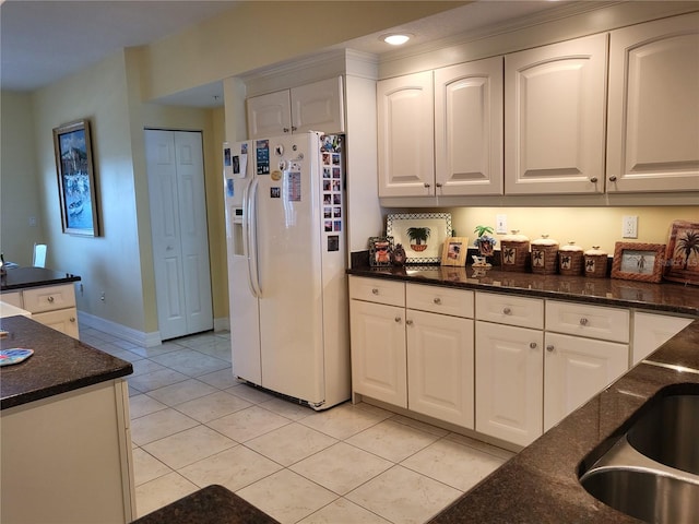 kitchen featuring light tile floors, white cabinets, dark stone counters, and white refrigerator with ice dispenser