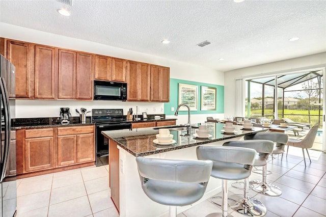 kitchen featuring sink, a kitchen breakfast bar, dark stone countertops, a center island with sink, and black appliances