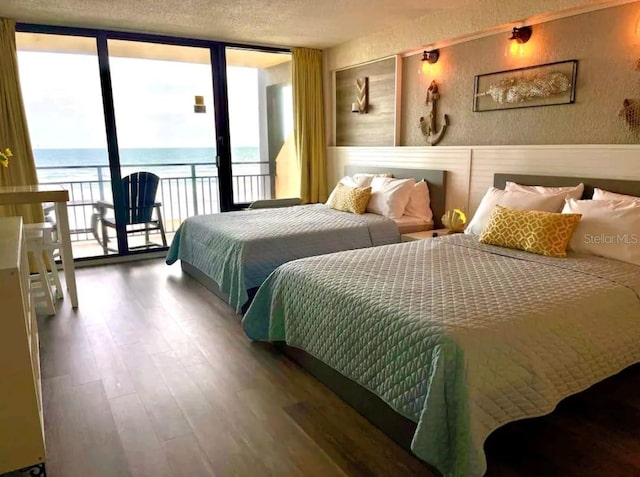 bedroom with hardwood / wood-style floors, expansive windows, access to outside, a water view, and a textured ceiling