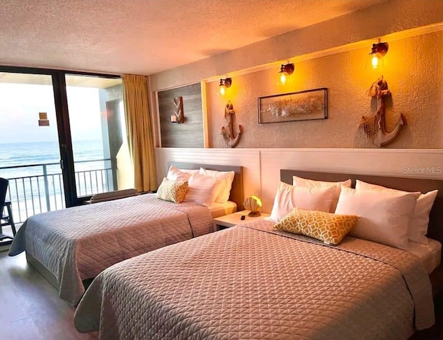 bedroom featuring expansive windows, dark hardwood / wood-style floors, access to exterior, a water view, and a textured ceiling