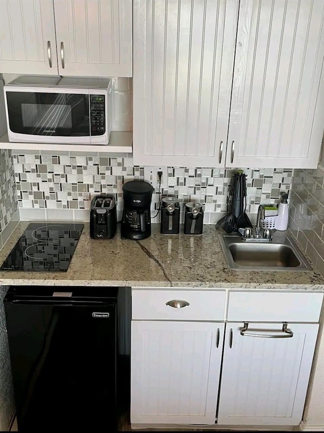 kitchen with backsplash, white cabinets, sink, and black appliances