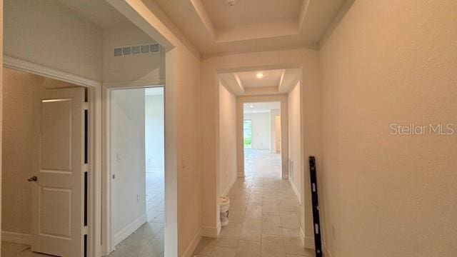 hall with visible vents, a tray ceiling, and baseboards