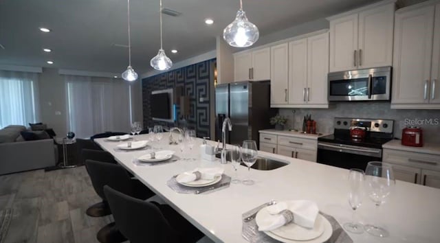 kitchen with an island with sink, pendant lighting, a kitchen bar, appliances with stainless steel finishes, and backsplash