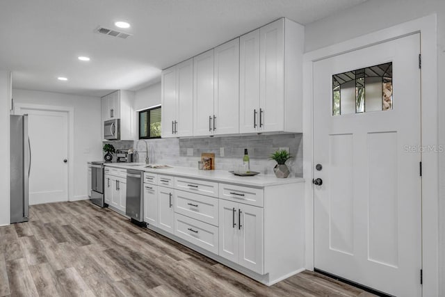 kitchen with white cabinets, backsplash, light wood-type flooring, and stainless steel appliances