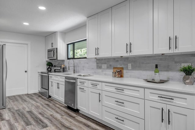 kitchen with appliances with stainless steel finishes, white cabinetry, backsplash, and light hardwood / wood-style flooring