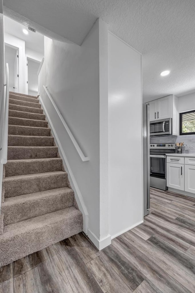 staircase with a textured ceiling and light wood-type flooring