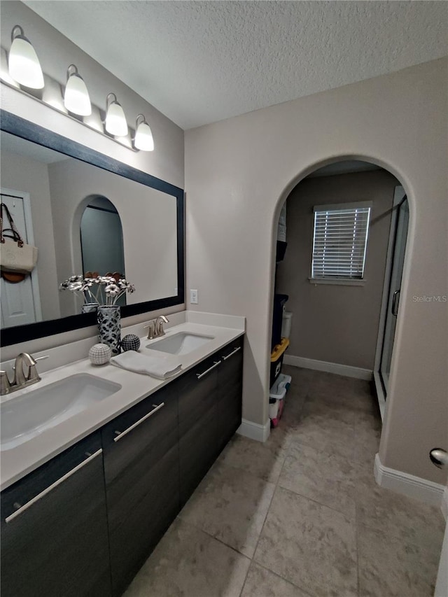 bathroom featuring a textured ceiling, tile flooring, and dual bowl vanity