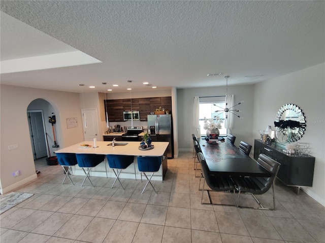 kitchen featuring light tile floors, a kitchen breakfast bar, appliances with stainless steel finishes, a center island with sink, and dark brown cabinetry