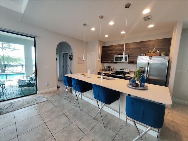 kitchen with a breakfast bar area, appliances with stainless steel finishes, dark brown cabinetry, a kitchen island with sink, and sink