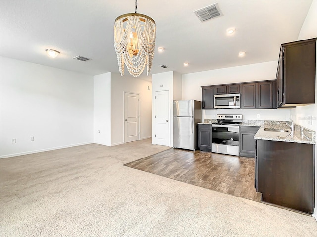 kitchen with an inviting chandelier, sink, stainless steel appliances, light carpet, and light stone counters