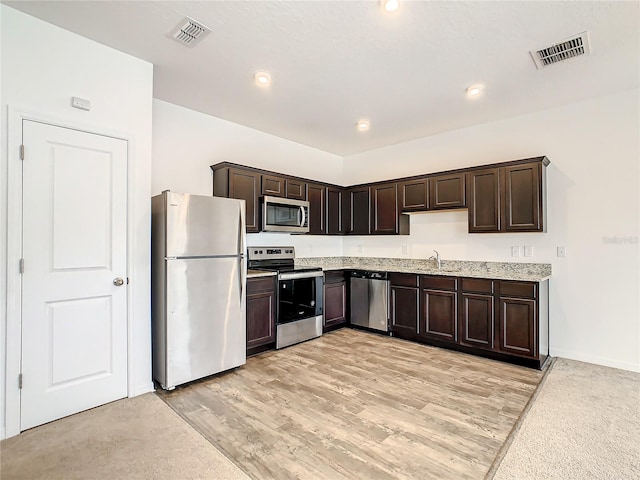 kitchen with appliances with stainless steel finishes, dark brown cabinetry, sink, and light hardwood / wood-style flooring