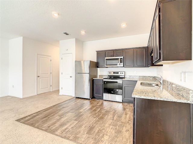 kitchen with sink, light wood-type flooring, stainless steel appliances, light stone countertops, and dark brown cabinetry