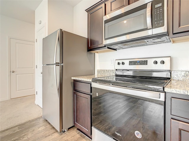 kitchen with light carpet, stainless steel appliances, dark brown cabinets, and light stone counters