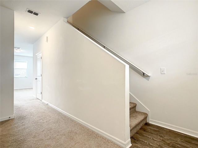 stairway featuring dark colored carpet