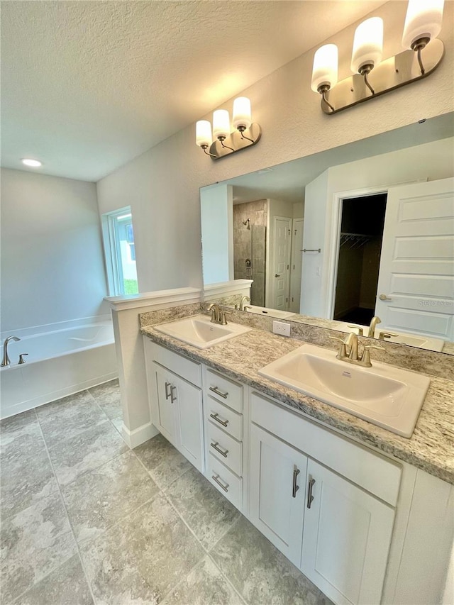 bathroom with a tub, dual sinks, tile flooring, a textured ceiling, and vanity with extensive cabinet space