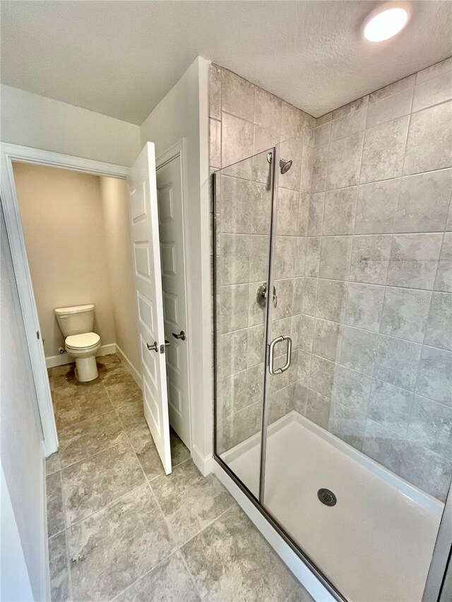 bathroom with toilet, a textured ceiling, a shower with door, and tile flooring