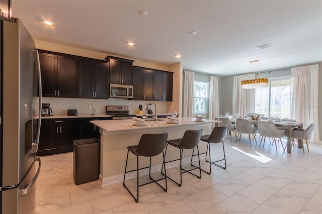 kitchen with hanging light fixtures, a kitchen island with sink, an inviting chandelier, appliances with stainless steel finishes, and a breakfast bar area