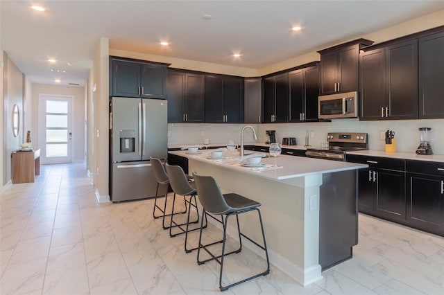 kitchen featuring a breakfast bar area, a center island with sink, appliances with stainless steel finishes, and light tile floors