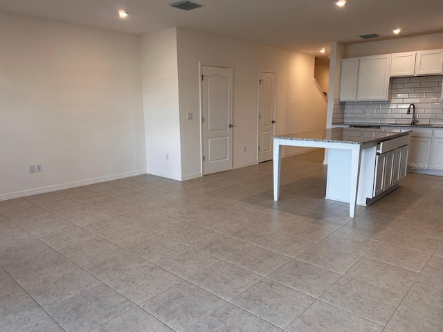 kitchen with sink, a center island, dark stone counters, decorative backsplash, and white cabinets