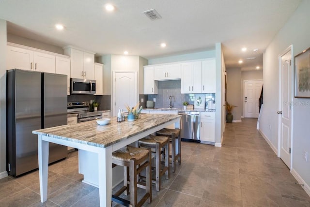 kitchen with a center island, a kitchen breakfast bar, stainless steel appliances, light stone countertops, and white cabinets