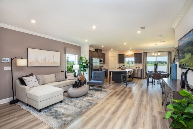 living room featuring ornamental molding, plenty of natural light, light hardwood / wood-style floors, and a notable chandelier