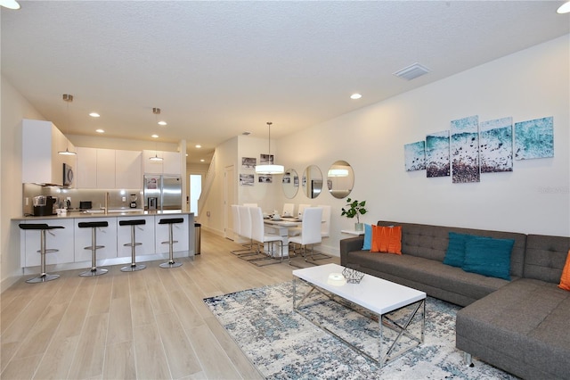 living room featuring a textured ceiling, sink, and light wood-type flooring