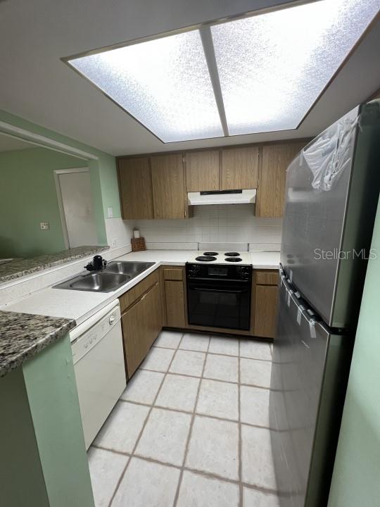 kitchen with kitchen peninsula, sink, black appliances, light tile patterned flooring, and tasteful backsplash